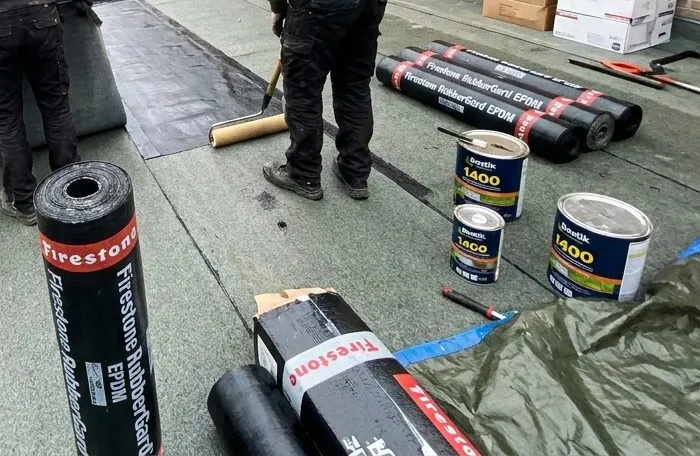 Rouleaux de membrane EPDM et pots de colle sur un toit plat en cours d'étanchéité à Rhode-Saint-Genèse